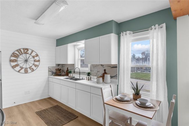 Kitchen with wood walls, white cabinetry, sink, light hardwood / wood-style floors, and a textured ceiling | Image 6
