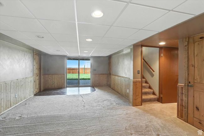 Carpeted basement living room room with a wainscoted wall, stairs, a wood paneled ceiling, and recessed lighting | Image 21