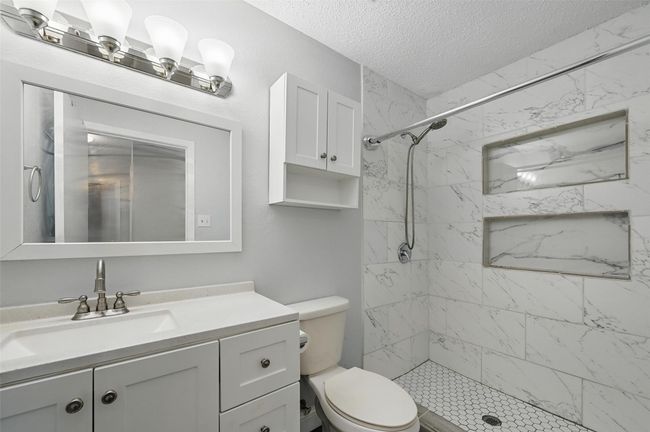 Bathroom with a textured ceiling, vanity, and a marble finish shower | Image 15