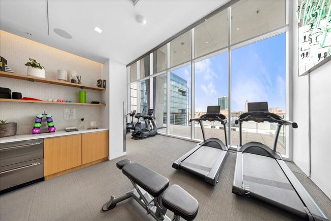 Exercise room featuring a wall ofAMENITIES. Elevated amenity deck on the tenth floor includes: Covered Lap Pool, Outdoor Cooking & Dining, Fire Pit Lounge, Sauna, Hot & Cold Plunge Pool, Exercise Facility, Dog Park w/ Washing Station, Conference Room / Private Dining, Club Room w/ Kitchen. Ground floor amenities include 24/7 Concierge, Lobby and two (2) retail spaces. windows and a city view | Image 22