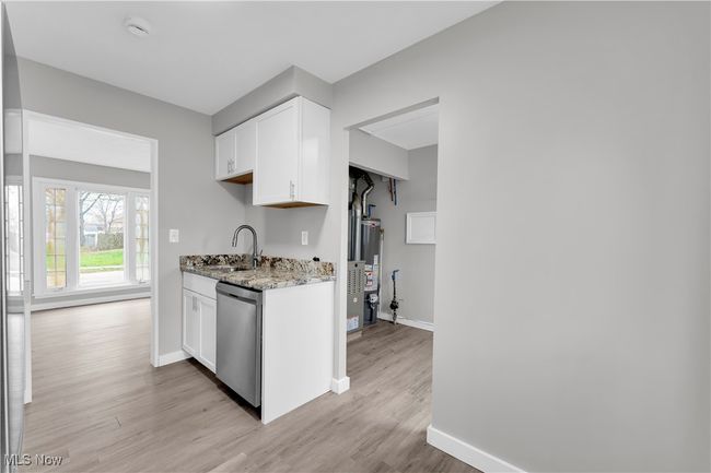 Kitchen with light stone countertops, a sink, light wood-style floors, stainless steel dishwasher, and white cabinets | Image 8