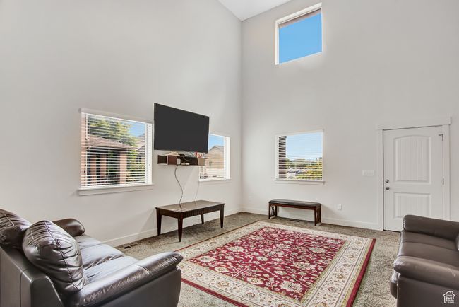 Carpeted living area featuring a high ceiling and baseboards | Image 9