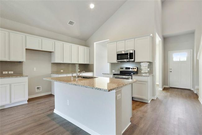 Kitchen featuring appliances with stainless steel finishes, white cabinetry, tasteful backsplash, high vaulted ceiling, and an island with sink | Image 6