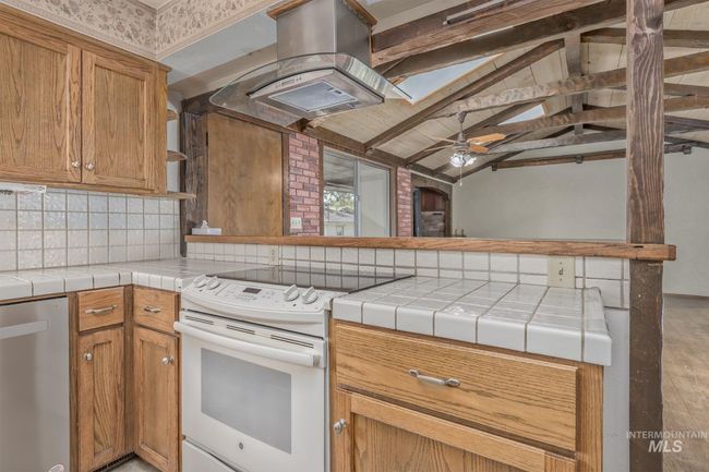 Kitchen featuring white range with electric stovetop, stainless steel dishwasher, tasteful backsplash, island exhaust hood, and ceiling fan | Image 10