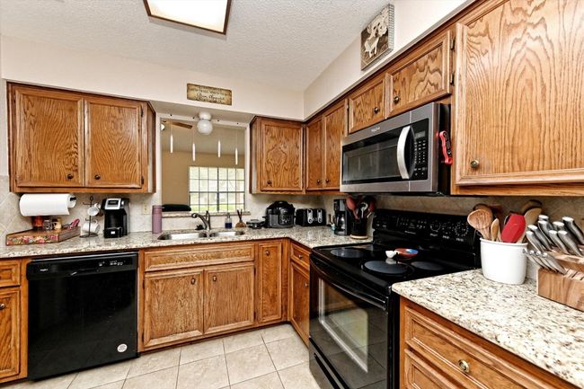 Kitchen with brown cabinetry, a stainless steel sink, black appliances, backsplash, and light tile patterned floors | Image 10