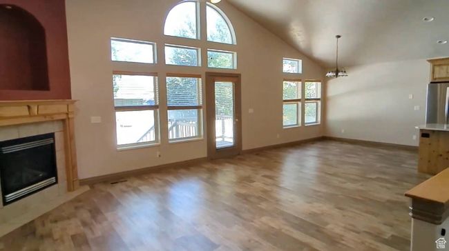 Unfurnished living room featuring healthy amount of natural light, light wood-type flooring, baseboards, and high vaulted ceiling | Image 7