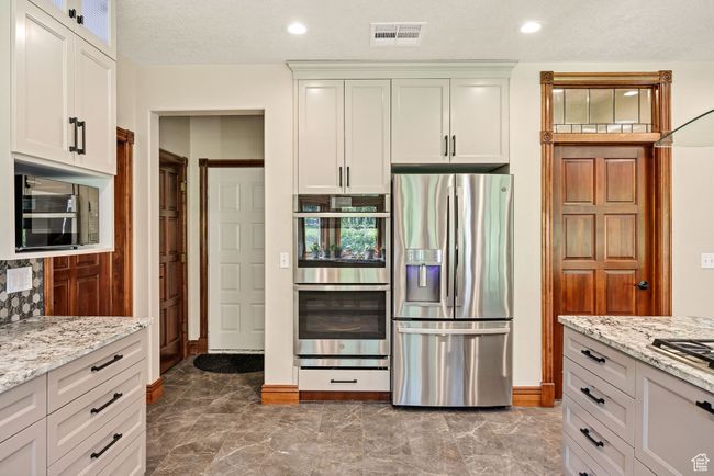 Kitchen with stainless steel appliances, marble finish flooring, light stone countertops, white cabinets, and recessed lighting | Image 6