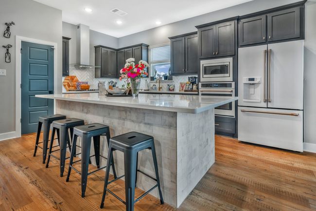 Kitchen featuring appliances with stainless steel finishes, wall chimney range hood, a large island, backsplash, and recessed lighting | Image 8