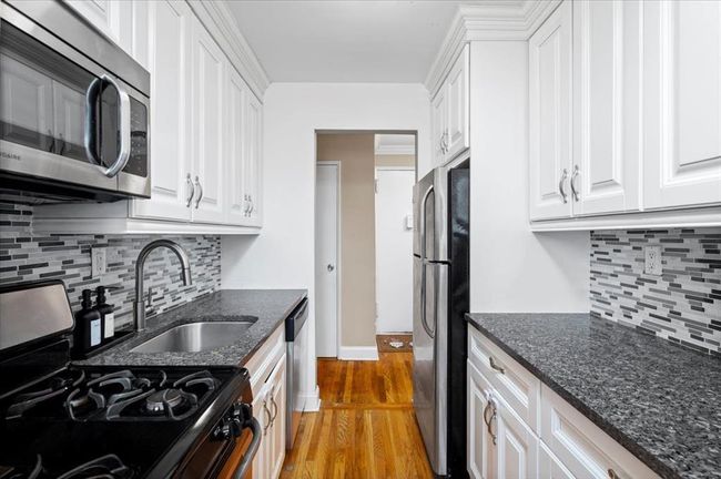 Kitchen with appliances with stainless steel finishes, white cabinets, light wood finished floors, and decorative backsplash | Image 12