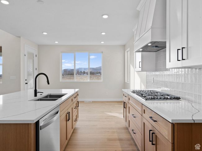 Kitchen featuring custom exhaust hood, stainless steel appliances, white cabinetry, a sink, and light stone countertops | Image 11