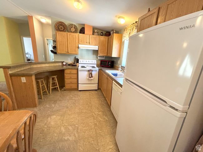 Kitchen featuring white appliances, under cabinet range hood, a sink, a peninsula, and a breakfast bar area | Image 24