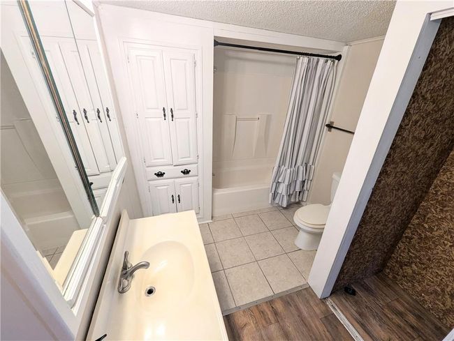 Full bathroom featuring a sink, a textured ceiling, toilet, shower / bath combo with shower curtain, and wood finished floors | Image 20