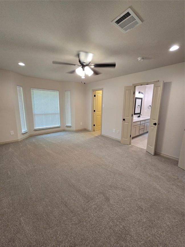 Primary bedroom featuring bay window, light colored carpet, recessed lighting, and a ceiling fan with doorways to closet and bathroom | Image 10