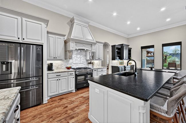 Kitchen featuring stainless steel fridge with ice dispenser, gas range oven, wall chimney range hood, light wood finished floors, and backsplash | Image 13