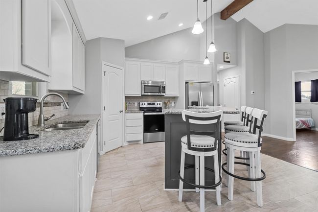 Kitchen featuring white cabinetry, stainless steel appliances, a center island, a sink, and beam ceiling | Image 7