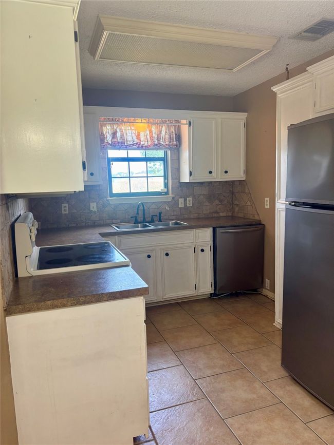 Kitchen with appliances with stainless steel finishes, white cabinets, decorative backsplash, dark countertops, and light tile patterned floors | Image 8
