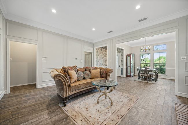 Living room with crown molding, a decorative wall, visible vents, a chandelier, and wood finished floors | Image 6