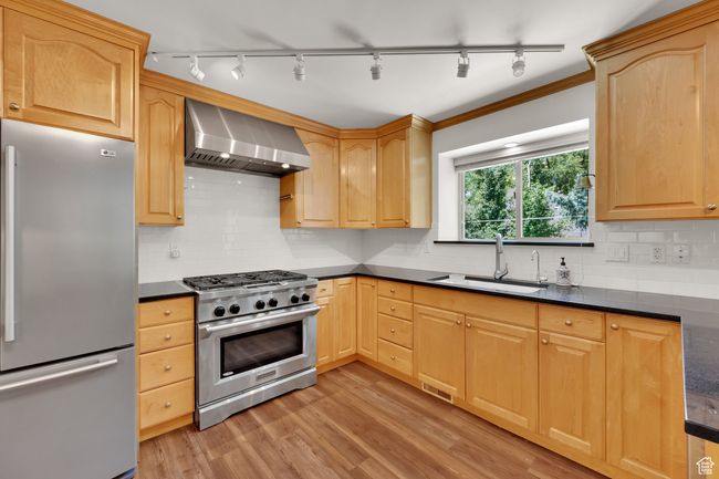 Kitchen featuring appliances with stainless steel finishes, wall chimney exhaust hood, dark countertops, a sink, and rail lighting | Image 10