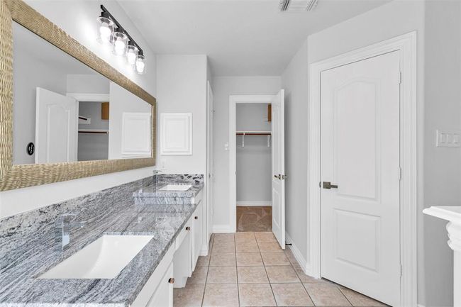 This bathroom features a dual-sink vanity with a sleek granite countertop, modern lighting, and ample storage space. The light-colored tile flooring complements the neutral wall tones, and there's a spacious walk-in closet for convenience. | Image 30