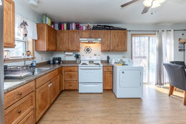 Kitchen with a sink, ceiling fan, under cabinet range hood, washer / dryer, and electric range | Image 30