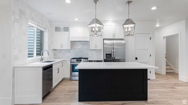 Kitchen featuring a sink, white cabinetry, custom range hood, a kitchen island, and appliances with stainless steel finishes | Image 61
