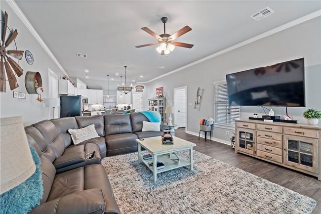 Living room with dark wood-style floors, ornamental molding, ceiling fan with notable chandelier, and visible vents | Image 20