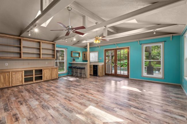 This bright and spacious game/ flex room has exposed beams, featuring large windows and French doors for ample natural light. The room includes built-in wooden shelving and cabinets, a wet bar area, creating a versatile and inviting space. | Image 19