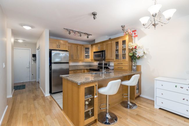 Kitchen with brown cabinets, light wood-style floors, glass insert cabinets, a peninsula, and appliances with stainless steel finishes | Image 9