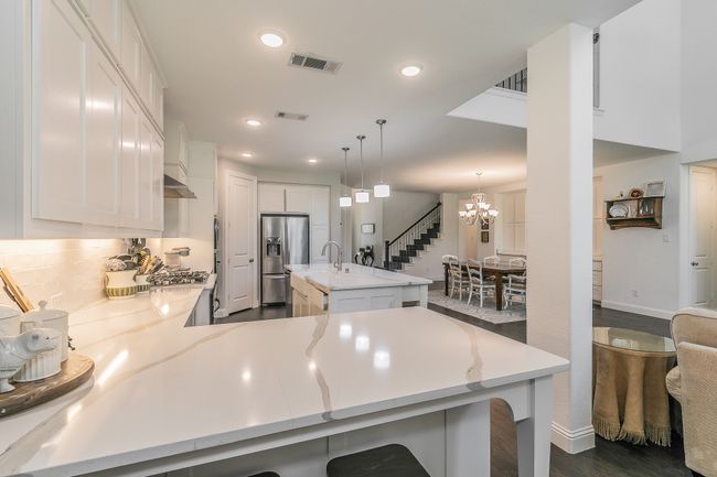 Kitchen with a chandelier, white cabinets, stainless steel fridge with ice dispenser, a kitchen bar, and recessed lighting | Image 5