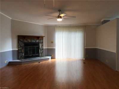 Living Room: Features include LVP flooring for easy cleaning, decorative chair rail and wainscoting, sliding patio door to backyard and deck, 3 windows for natural lighting with blinds for privacy, fresh new paint, 2 new ceiling fans with lights and decorative crown molding. The fireplace is wood burning and should be professionally inspected before using. | Image 2