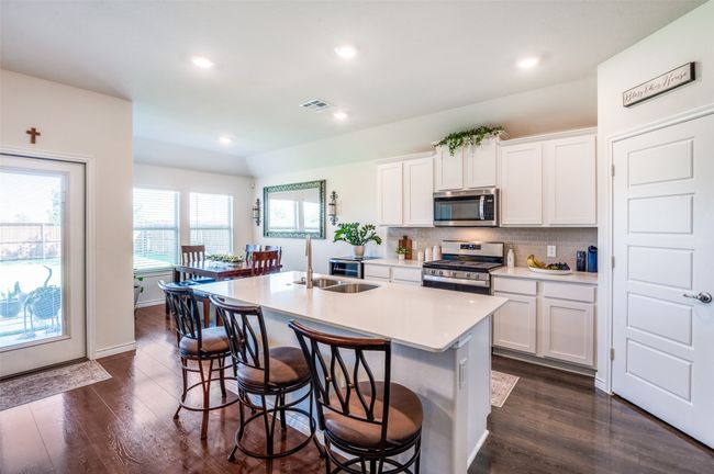 Kitchen featuring appliances with stainless steel finishes, a center island with sink, dark wood-style flooring, tasteful backsplash, and recessed lighting | Image 11