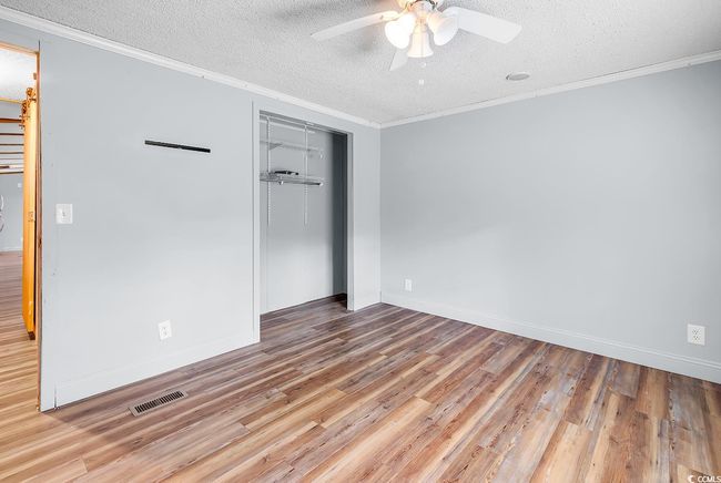 Unfurnished room featuring a textured ceiling, crown molding, ceiling fan, wood finished floors, and baseboards | Image 25