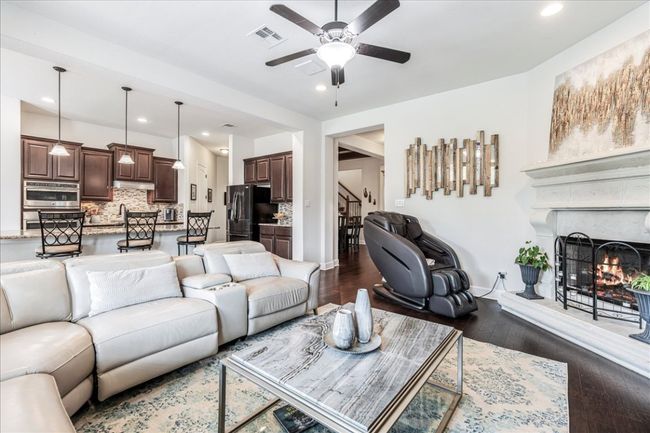 Living room featuring recessed lighting, dark wood finished floors, a warm lit fireplace, ceiling fan, and stairs | Image 11