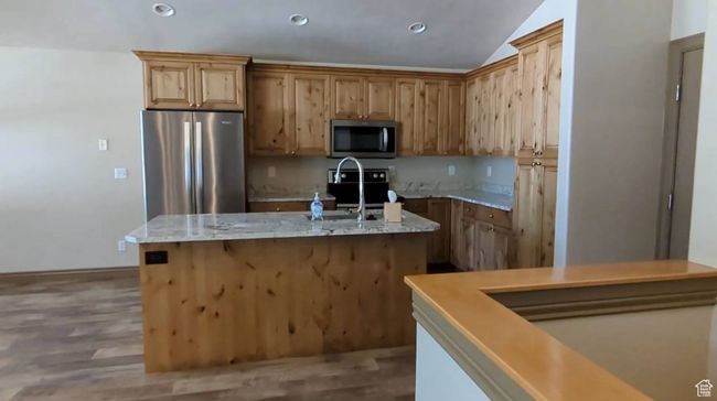 Kitchen with stainless steel appliances, a kitchen island with sink, vaulted ceiling, wood finished floors, and light stone counters | Image 15