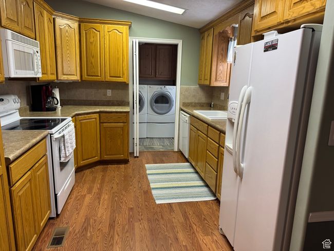 Kitchen featuring white appliances, washer and clothes dryer, dark wood-style flooring, vaulted ceiling, and tasteful backsplash | Image 7