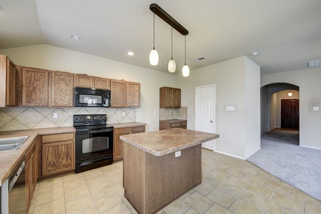 Kitchen featuring tasteful backsplash, black appliances, brown cabinetry, decorative light fixtures, and recessed lighting | Image 12