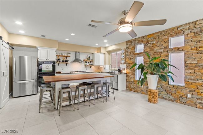Kitchen with stainless steel appliances, butcher block counters, a sink, wall chimney exhaust hood, and open shelves | Image 12