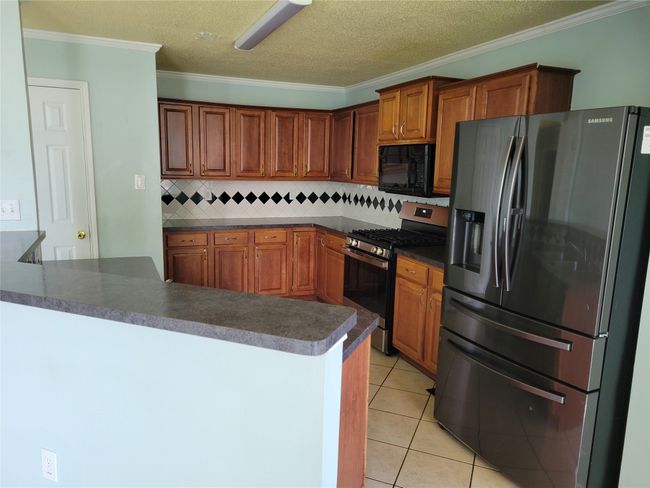 Kitchen with refrigerator with ice dispenser, stainless steel range with gas cooktop, black microwave, dark countertops, and decorative backsplash | Image 5