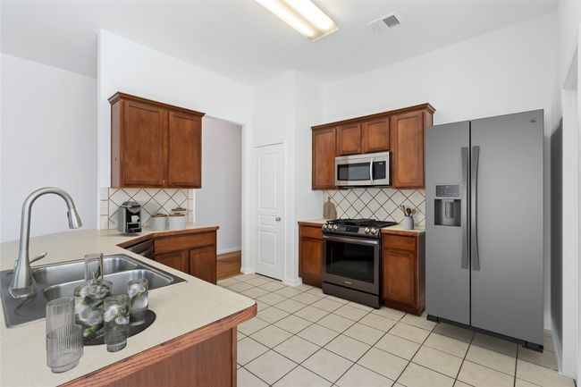 Kitchen with stainless steel appliances, tasteful backsplash, light countertops, light tile patterned floors, and a peninsula | Image 11