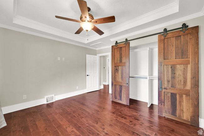 Unfurnished bedroom with visible vents, dark wood-type flooring, a raised ceiling, and a barn door | Image 12