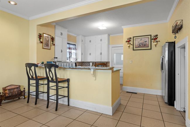 Kitchen with a peninsula, crown molding, a kitchen bar, white cabinets, and freestanding refrigerator | Image 10