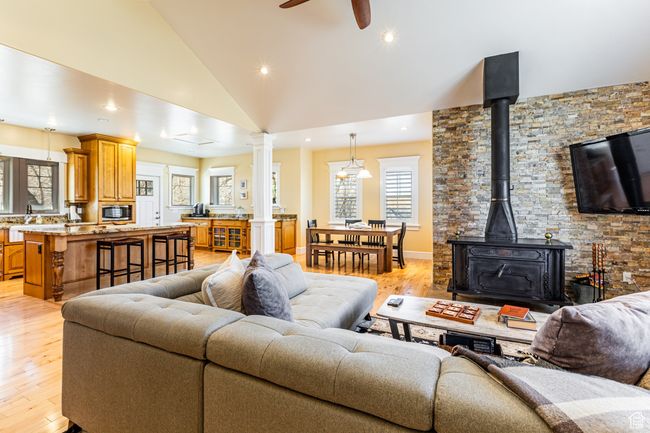 Living area with high vaulted ceiling, light wood-style floors, a wood stove, and ceiling fan | Image 4
