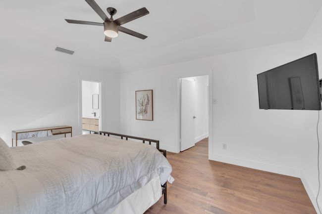 Bedroom featuring a ceiling fan, visible vents, wood finished floors, baseboards, and ensuite bath | Image 23