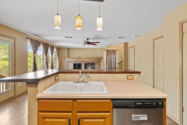 Kitchen featuring open floor plan, dishwasher, a center island with sink, a ceiling fan, and hanging light fixtures | Image 12