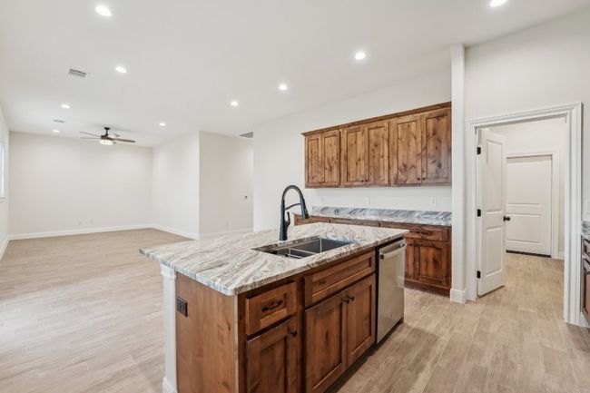 Kitchen featuring a center island with sink, dishwasher, wood plank tile floor, a ceiling fan, and a sink | Image 15