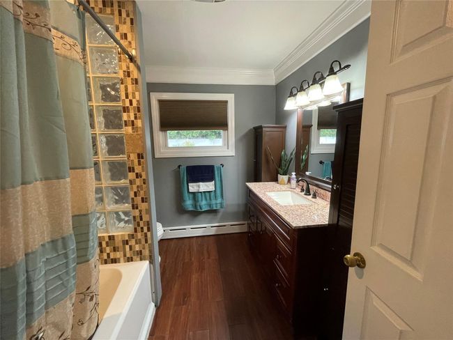 Bathroom featuring baseboard heating, crown molding, vanity, wood finished floors, and plenty of natural light | Image 28