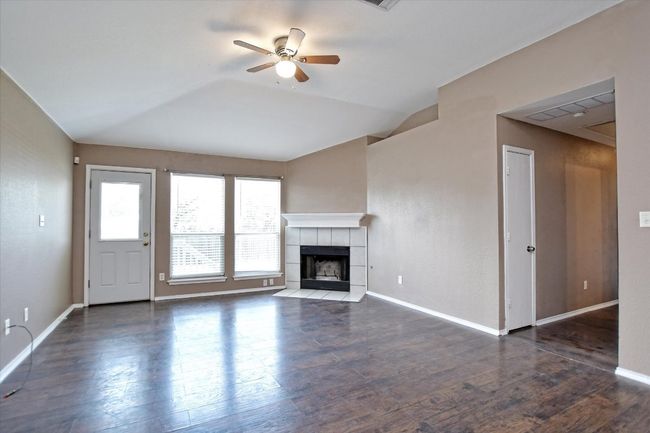 Unfurnished living room featuring a ceiling fan, a tile fireplace, lofted ceiling, wood finished floors, and baseboards | Image 9