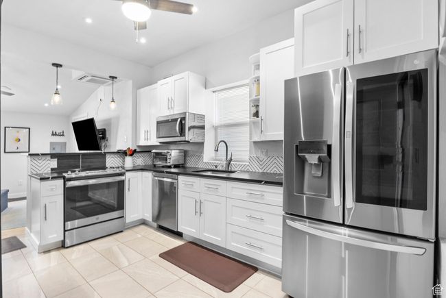Kitchen with a peninsula, white cabinetry, dark countertops, appliances with stainless steel finishes, and a sink | Image 24