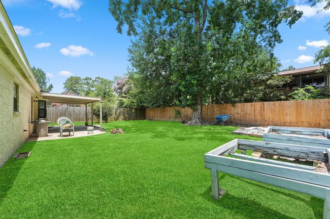 This spacious backyard features a well-maintained lawn, a large tree providing shade, a covered patio area for relaxation, and raised garden beds. It's perfect for outdoor activities and gardening. | Image 25