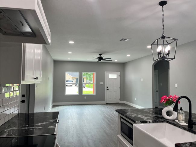 Kitchen featuring stainless steel microwave, white cabinets, range hood, wood finished floors, and ceiling fan | Image 5
